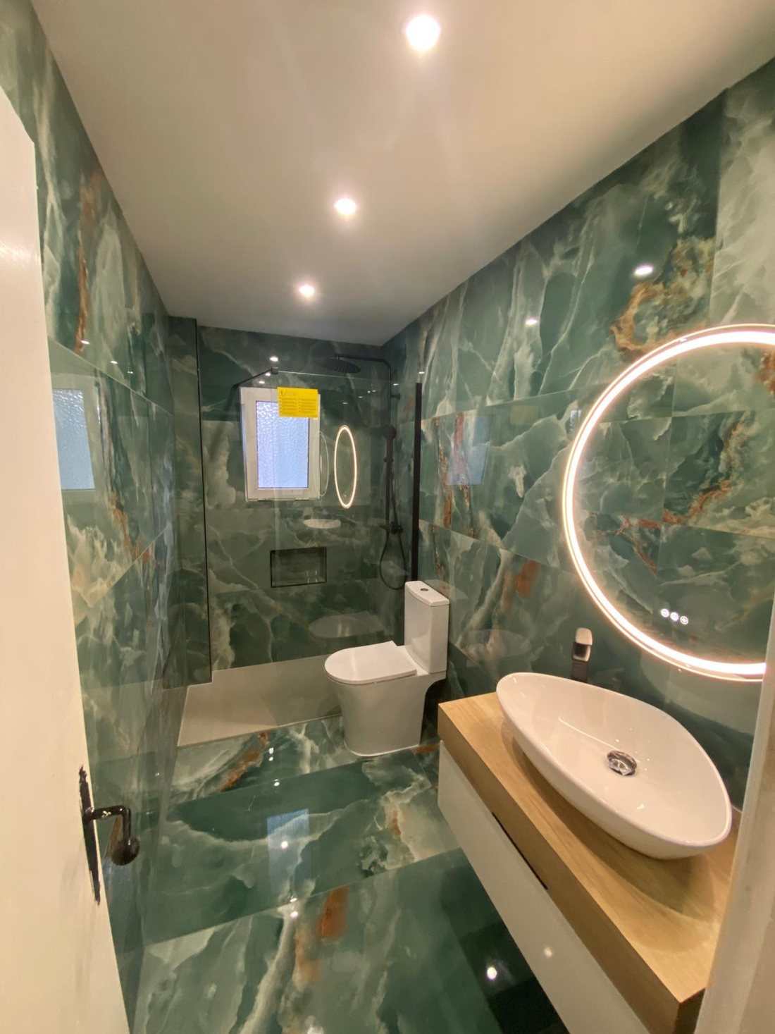 Baño terminado con revestimiento tipo ónice verde e iluminación LED